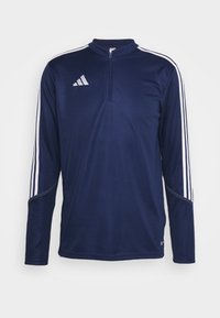 Námořnická modrá sportovní mikina s dlouhým rukávem, bílými pruhy na rukávech, čtvrtzipovým límcem a bílým logem Adidas na hrudi.