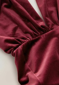 Burgunderroter Samtstoff mit gerafften Nähten, der eine glatte Textur und einen sanften Glanz aufweist und elegante Falten und Konturen erzeugt.
