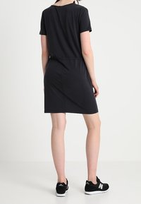 Robe noire à manches courtes avec une taille cintrée, de longueur mi-longue, douce au toucher et dotée d'un simple col rond, associée à des baskets noires.