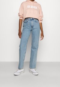 Sudadera corta de color rosa claro con el logo "LEVI'S", combinada con jeans de cintura alta de color azul claro y zapatillas de lona blancas.