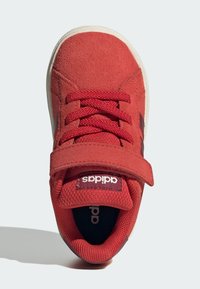 Crvene suede tenisice s vezicama i čičak trakama, podstavljenim ovratnikom i Adidas logotipom na jeziku i ulošku, prikazane iz gornjeg pogleda.
