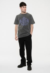 Gray cotton T-shirt with a vintage wash, featuring purple graphic print on the front. Paired with black pants and black shoes.