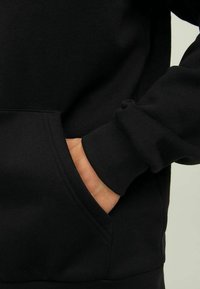 Felpa nera con tasca a marsupio, polsini a costine e una texture di tessuto morbida. Il design è minimalista e aderente.