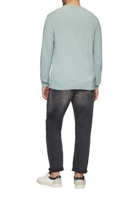Hellblauer Strickpullover mit raglanärmeln, kombiniert mit grauen Jeans und weißen Turnschuhen, im lässigen Schnitt und mit gerippten Bündchen.