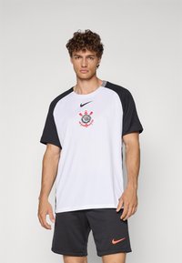 Nike sports skjorte med hvit kropp, svarte ermer og rød logo. Enkelt tekstur med rund hals og korte ermer. Svarte shorts med logo.