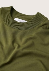 Bluza w oliwkowym kolorze z ribbowanym dekoltem. Wykonana z miękkiego materiału o gładkiej fakturze, z delikatnymi fałdami i zmarszczkami.