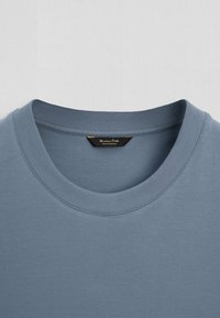 Sweat-shirt bleu à col rond avec col côtelé et étiquette de marque noire visible cousue à l’intérieur de l’encolure.