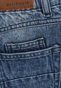 Denimjeans med medeltvätt, som har en framficka och en läderetikett präglad med "EN·FANT." Sömmarna är i kontrasterande mörkblå färg.