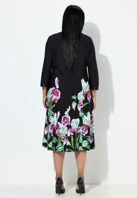 Czarna sukienka w kwiaty z rękawami do połowy łokcia, ozdobiona jaskrawymi fioletowymi i niebieskimi kwiatami oraz zielonymi liśćmi, sięgająca do połowy łydki.