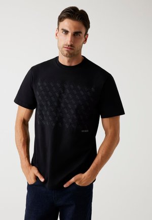 Zwarte katoenen T-shirt met een tonale diamantpatroon en het "GUESS" logo aan de onderzijde van de voorkant. Ronde halslijn, korte mouwen, ontspannen pasvorm.