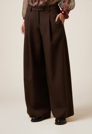 Pantalons larges en tissu marron riche avec une texture lisse, présentant des plis avant, une fermeture à bouton et des poches latérales.