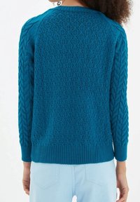 Kungsblå stickad tröja med strukturerade diamantmönster och kabelstickade ärmar. Ribbad nederkant och manschetter, med rundad halsringning och långa ärmar.