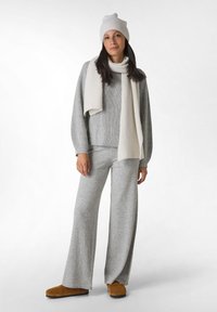 Maglione grigio chiaro a coste e pantaloni a gamba larga, abbinati a una sciarpa color crema e un berretto in maglia. Le pantofole marroni completano l'outfit accogliente.