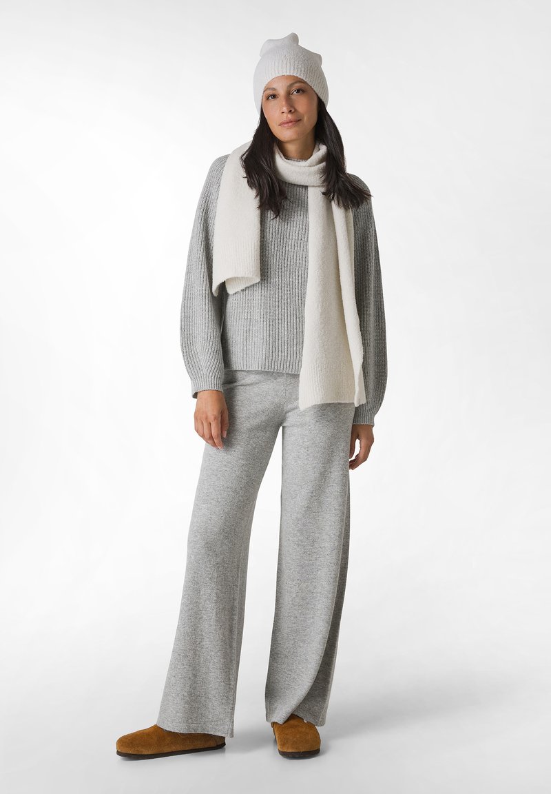 Maglione grigio chiaro a coste e pantaloni a gamba larga, abbinati a una sciarpa color crema e un berretto in maglia. Le pantofole marroni completano l'outfit accogliente.