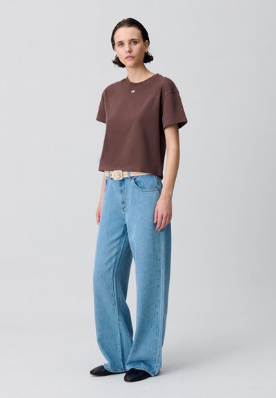 T-shirt marron court à manches courtes, assorti à un jean large bleu clair et une ceinture tissée beige, complété par des ballerines noires.
