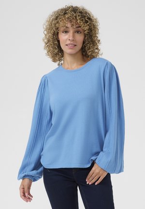 Lichtblauwe lange mouwen top van textuurstof met ballonmouwen, voorzien van een ronde halslijn en een ontspannen pasvorm, gecombineerd met donkere jeans.