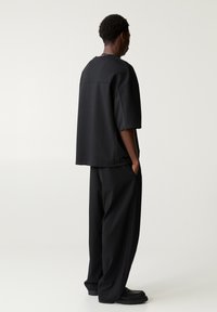 T-shirt nera oversize a maniche corte, con un retro testurizzato e cuciture piatte, abbinata a pantaloni neri larghi e scarpe nere chunky.
