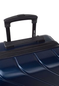 Maleta rígida en azul oscuro, con una superficie texturizada, asa negra y cierre de cremallera con detalle de marca en el asa.