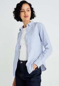 Πουκάμισο με κουμπιά σε μπλε και λευκές ρίγες, γιακά, μακριά μανίκια και άνετη εφαρμογή, συνδυασμένο με λευκό πουκάμισο και σκούρο τζιν.