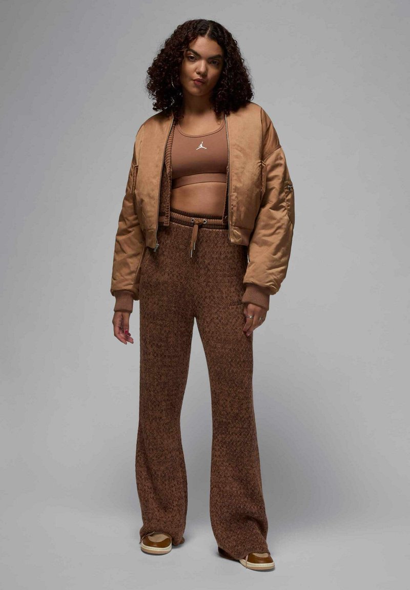 Veste bomber en satin bronze sur un crop top marron et un pantalon en tricot marron à la coupe ample, avec une taille élastique à cordon. Des baskets complètent l'ensemble.