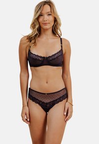 Soutien-gorge en dentelle noire et culottes assorties en tulle à pois. Le soutien-gorge présente des bords ondulés et des bretelles réglables. Les culottes ont une taille en dentelle florale.
