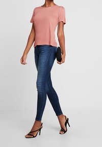 Lys rosa kortærmet T-shirt med en afslappet pasform, parret med mørkeblå skinny jeans og sorte strop sandaler med høj hæl. Kompakt sort pung.