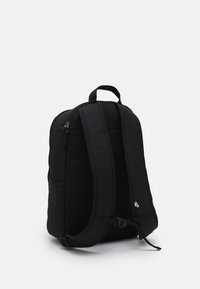 Zaino nero realizzato in tessuto resistente con retro imbottito e spallacci regolabili. Presenta una tasca con zip e un piccolo dettaglio con logo.
