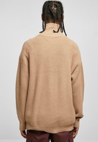 Beige, stor oversized genser med ribbet tekstur, høy krage og senkede skuldre. Designet har en avslappet passform og lange ermer.