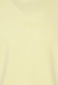 Camiseta de algodón color amarillo claro con una textura suave y el logo en relieve "YPS" en un color a juego en la parte delantera. Diseño simple y minimalista.