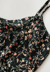 Robe noire sans manches avec fines bretelles et motif floral aux tons beige, corail et vert sur un tissu texturé.