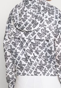 Czarna i biała kurtka z kapturem z całkowitym wzorem abstrakcyjnym. Posiada elastyczny ściągacz w dolnej części i na mankietach, wykonana jest z gładkiego, lekkiego materiału.