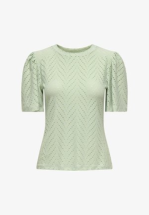 Krótki rękaw, zielona bluzka uszyta z teksturowanej tkaniny, z wycięciami w zygzaki i marszczonymi ramionami, z okrągłym dekoltem i dopasowanym krojem.