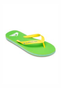 Grøn flip-flop med gule stropper, der har en tekstureret sål og subtile flerfarvede accentlinjer nær kanten. Logoet er synligt på indersiden.