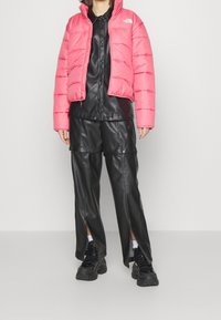 Giacca puffer rosa con design a trapunta orizzontale, camicia e pantaloni in pelle nera, con orli aperti, abbinati a sneakers nere chunky.