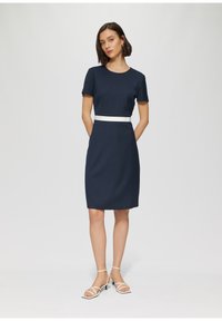 Vestito blu navy con maniche corte, silhouette aderente e cintura bianca in vita. Tessuto liscio, lunghezza al ginocchio e motivi minimi.