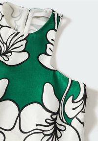 Robes sans manches avec un grand motif floral vert et blanc souligné de noir, col haut et fermeture éclair au dos.