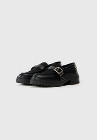 Fekete loaferek, textúrált felső résszel, dekoratív csattal, masszív fekete talppal és fényes kivitelben. Könnyű és slip-on dizájn.
