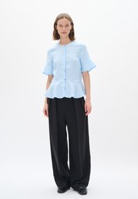 Svetle modrý peplum top s krátkými volánkovými rukávy a zapínáním na knoflík, zkombinovaný s vysokými černými kalhotami s širokými nohavicemi. Hladká textura látky.