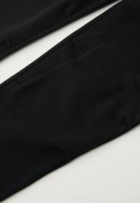 Čierne legíny vyrobené z mäkkého, elastického materiálu. Majú hladkú textúru, priliehavý strih a malú látkovú nášivku na boku.