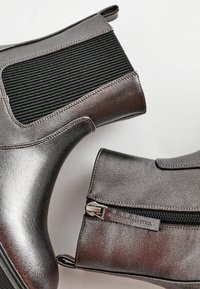 Bottines gris métallique avec des panneaux élastiques noirs côtelés, des zips sur les côtés et une finition en cuir lisse. Présente des coutures et des languettes de tirage.