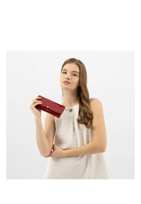 Portafoglio rosso con stampa a croco e accentuazione in logo argentato, caratterizzato da una forma rettangolare elegante e una finitura lucida, tenuto da un modello.