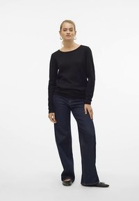 Maglione nero a maniche lunghe con scollo rotondo, abbinato a jeans scuri a zampa e ballerine nere, con una texture liscia.