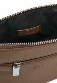 Portafoglio in pelle marrone con una superficie testurizzata, impermeabile con zip in argento e fodera interna nera con un motivo di logo ripetuto.