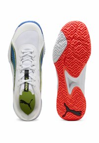 Zapatilla deportiva Puma blanca con detalles laterales en azul y amarillo, plantilla verde, cordones blancos y suela roja con patrón y logo de Puma en negro.