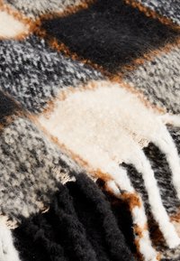 Tissu en laine douce avec un motif à carreaux noir, gris, blanc et marron et des bords à franges.
