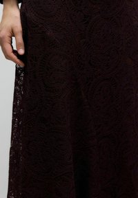 Pitsseelik sügavbordoopunases toonis, millel on keerukad keerutatud mustrid, tekstuuriga viimistlus ja voolav siluett, mida täiendab helplotis.