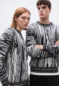 Pulls en tricot noirs et blancs, présentant des motifs abstraits en forme de vague. Les deux ont des encolures rondes et des poignets et ourlets côtelés contrastants.