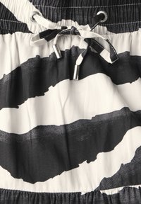 Tessuto in bianco e nero con audaci strisce a pennellate. Vita elasticizzata con cordoncino e punte metalliche per la regolazione.
