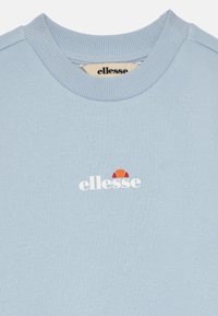Svijetloplava dukserica od pamuka, s rebrastim okruglim izrezom i bijelim "ellesse" logotipom s crvenim i narančastim naglascima iznad.