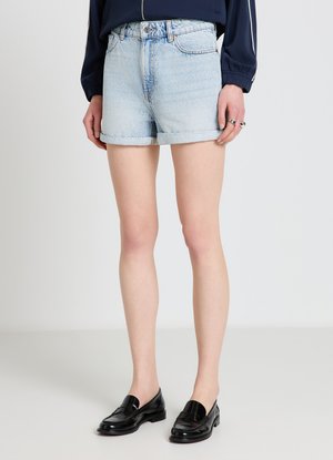 Short en jean bleu clair à ourlet roulé, porté avec des mocassins en cuir noir et un haut à manches longues bleu marine, présenté de la mi-cuisse jusqu'aux pieds.